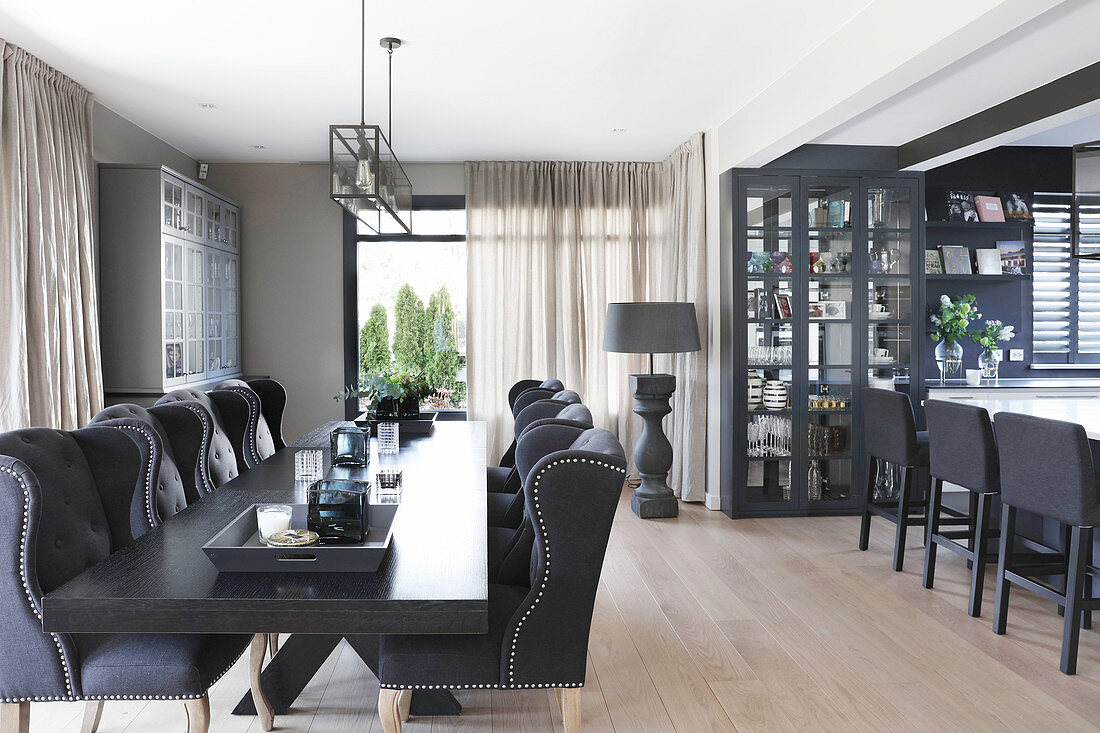 Elegante Polsterstühle um schwarzen Tisch im Essbereich, im Hintergrund Vitrinenschrank und Kücheninsel