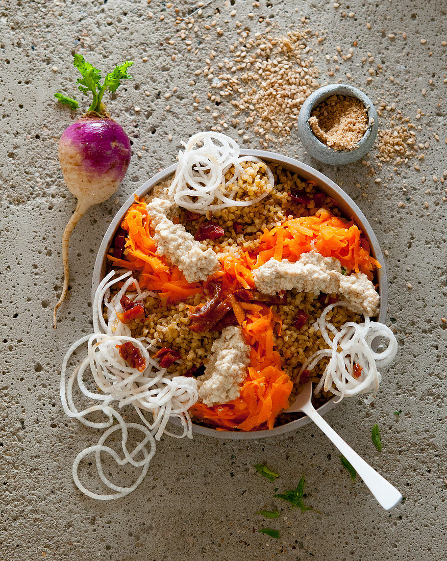 A bulgur bowl with radish, carrots, dried tomatoes and sesame seed cream cheese