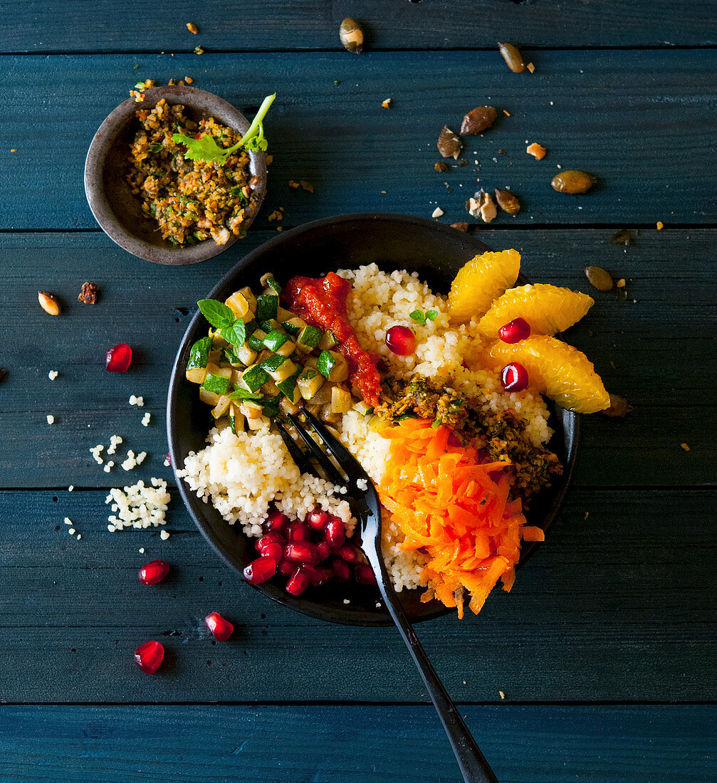 Oriental bowl with couscous, courgette, pomegranate seeds, carrots, oranges and pumpkin seeds