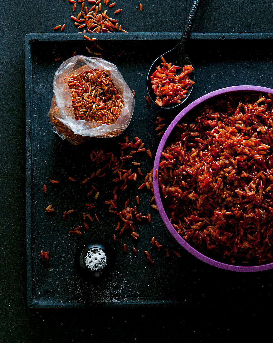 Roter gekochter Reis in Reisschale neben ungekochtem Roten Reis im Beutel