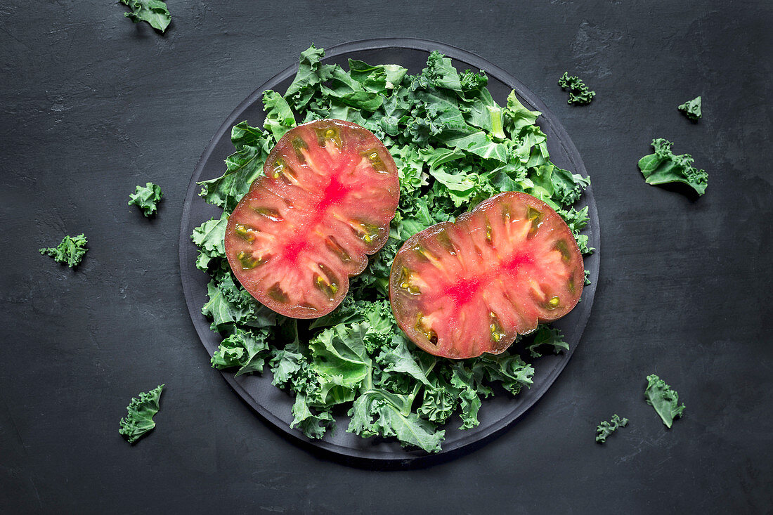 Slices of fresh tomatoes and torn lettuce leaves placed on plate against black plaster background