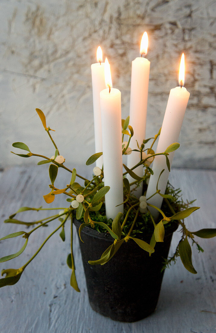 Four white candles in black pot with moss and mistletoe