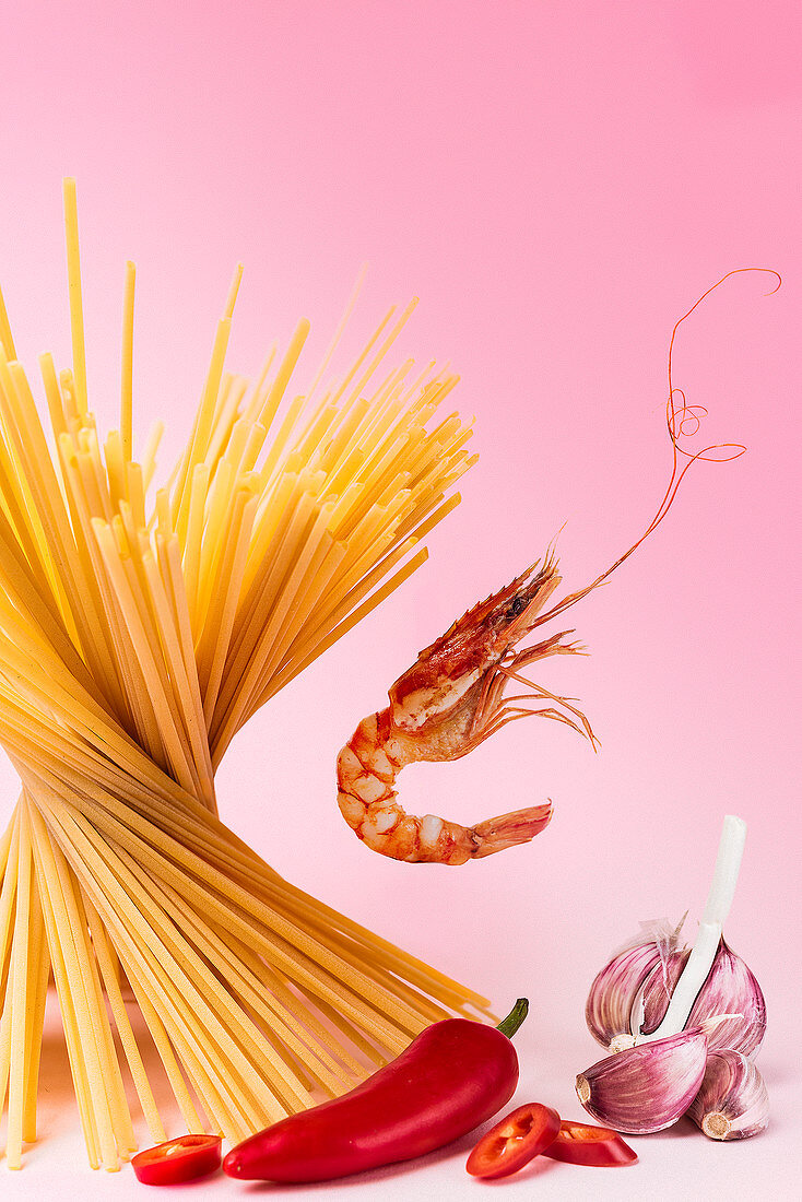 An arrangement of of spaghetti, a chilli pepper, garlic and prawns