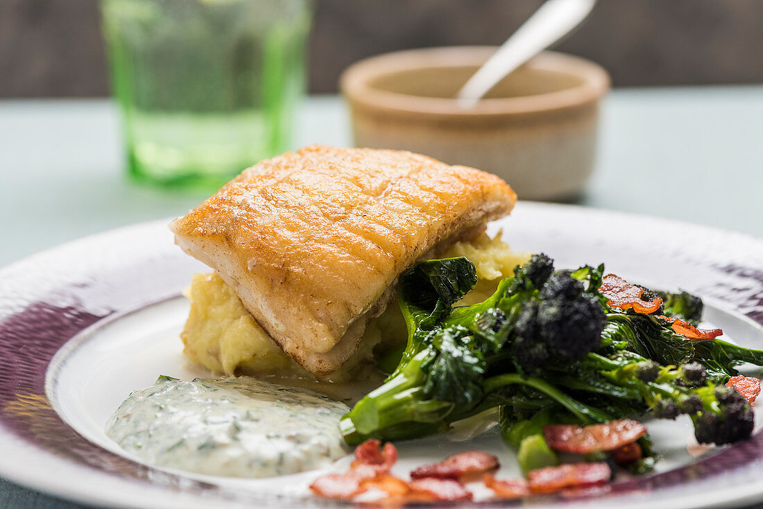 Fried fish on a bed of mashed potatoes with broccolini and herb sauce