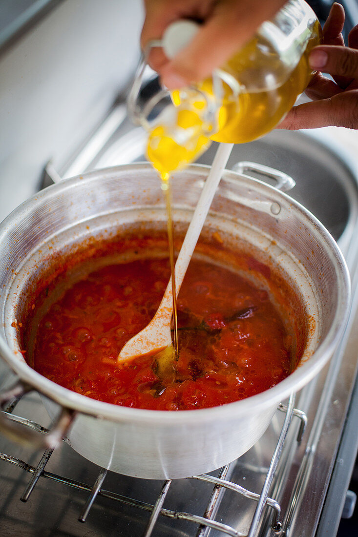 Tomato sugo being seasoned with olive oil