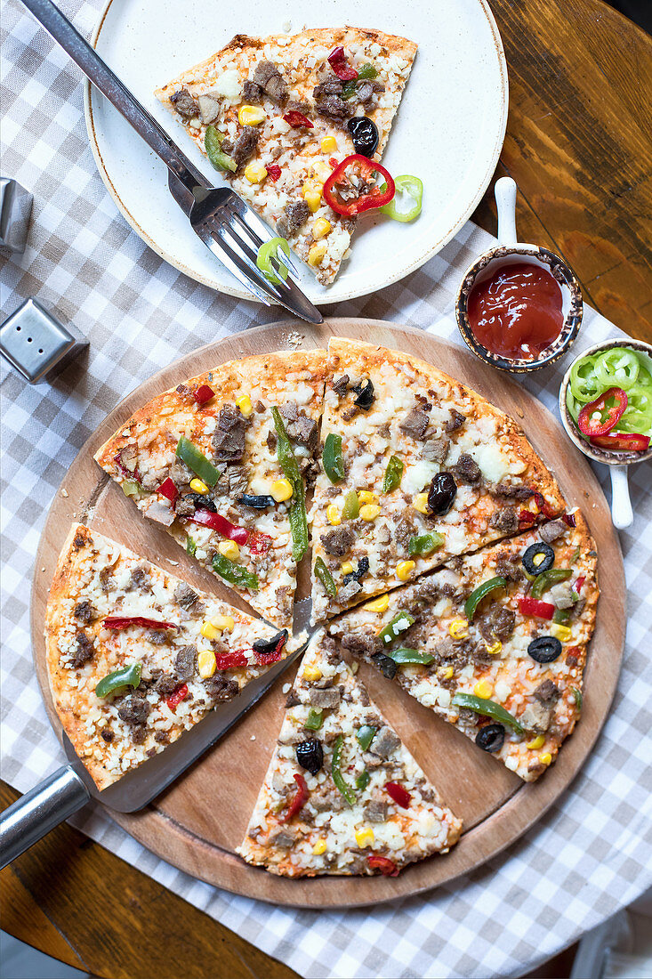 A pizza topped with meat, sweetcorn and vegetables