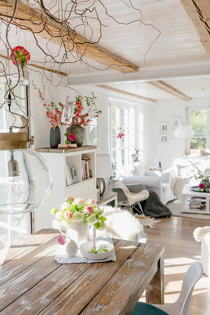Rustikaler Esstisch mit Blumenstrauß, im Hintergrund Lounge in offenem Wohnraum