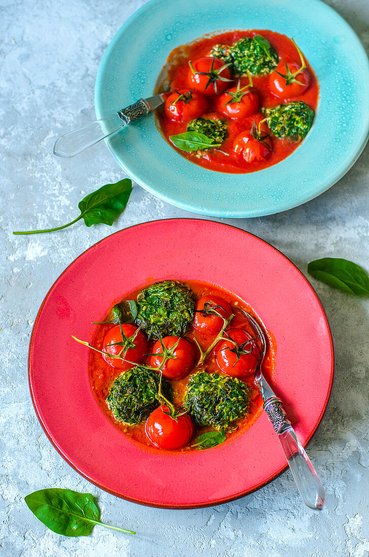 Spinach and ricotta cutlets with parmesan and garlic in tomato sauce with whole cherry tomatoes in red and blue plates