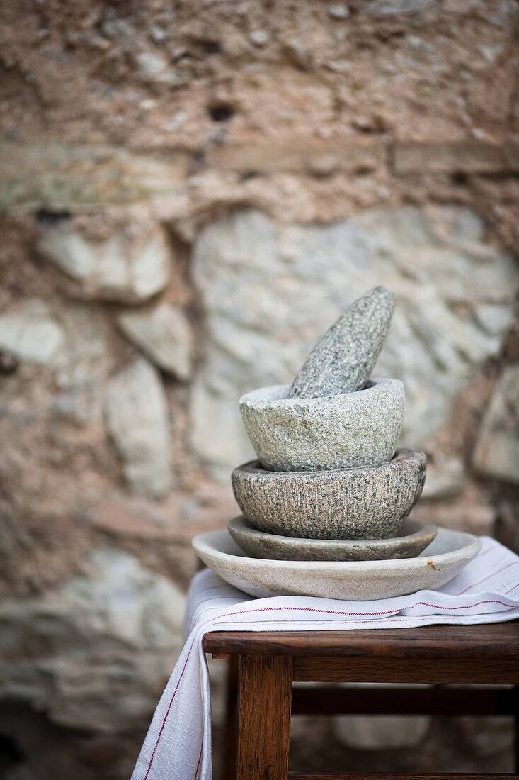 A stack of stone mortars with a pestle in front of a stone wall