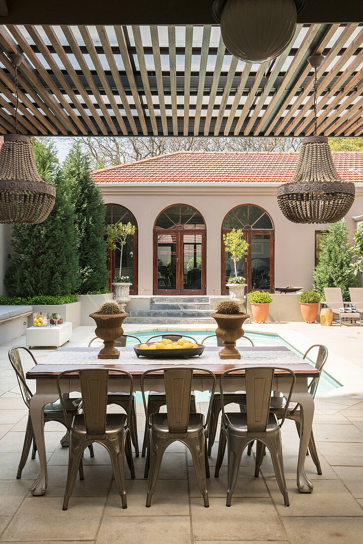 Esstisch mit Stühlen auf der Terrasse mit Sonnenschutz, im Hintergrund Pool