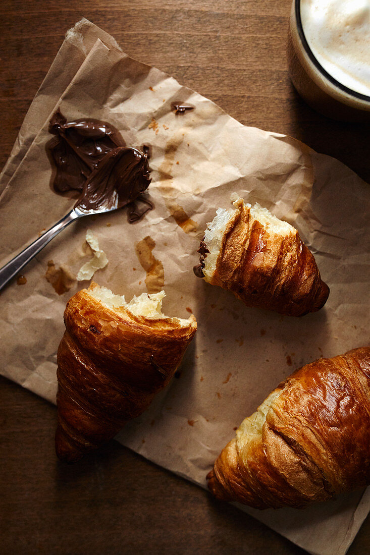 Zwei Croissants auf brauner Papiertüte mit Nusscreme und Kaffee