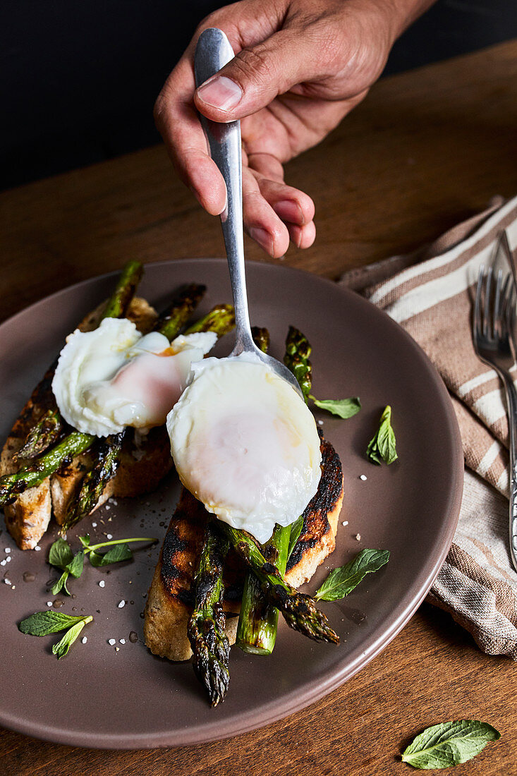 Putting poached egg on grilled asparagus and toasted bread