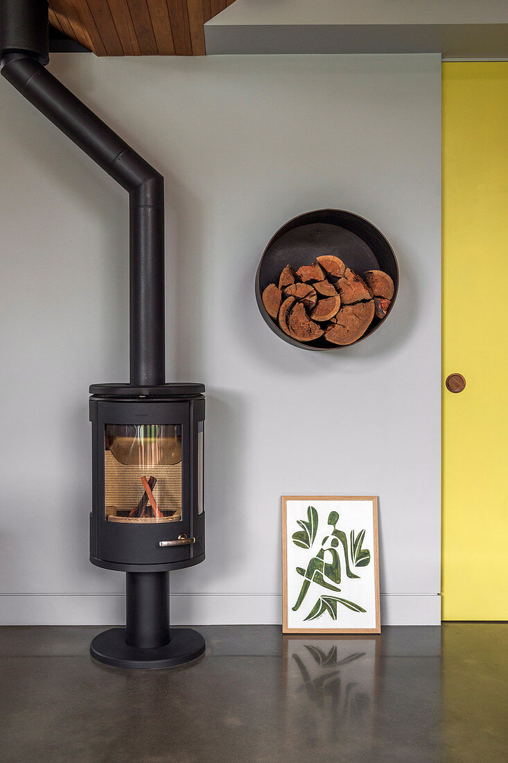 Modern Swedish stove with stovepipe next to a round shelf for firewood