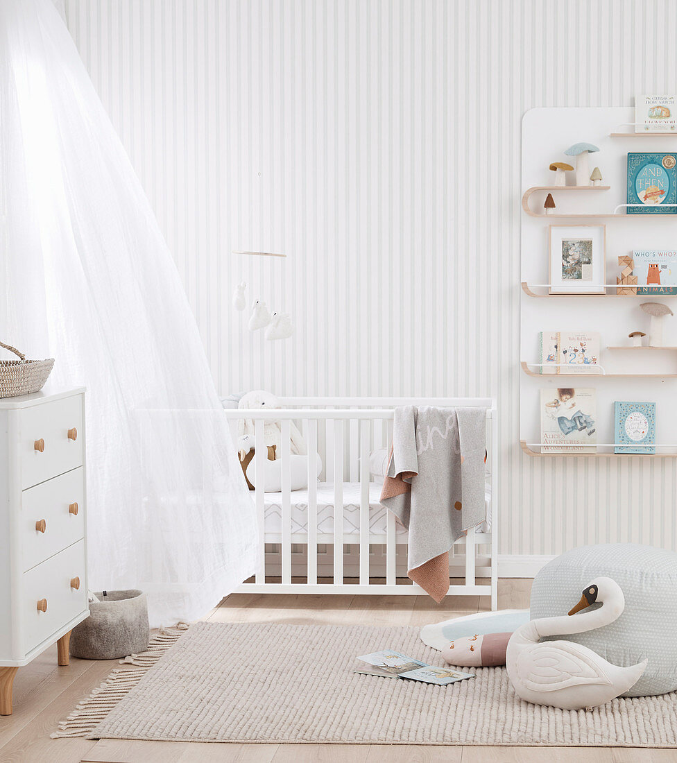 Babyzimmer in hellen Farben mit Gitterbett, Kommode und Wandregal