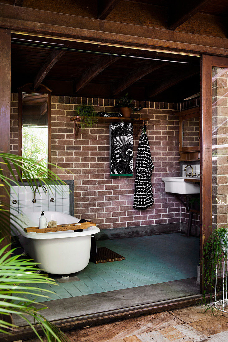 Vintage bathtub in front of a brick wall in a natural bathroom with a wide open sliding door