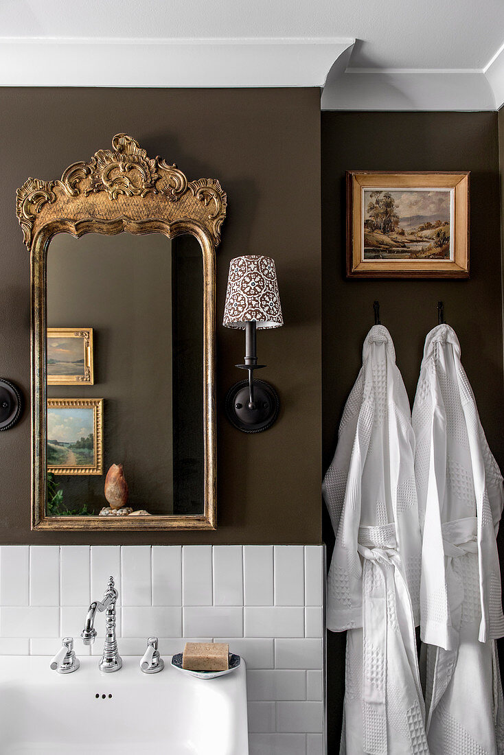 Gold frame mirror and umbrella wall lamp in a stylish bathroom with brown walls