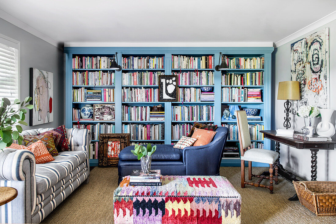 Wohnzimmer im Stilmix mit himmelblauer Bücherwand, Sofa, Ottoman und Polstertisch