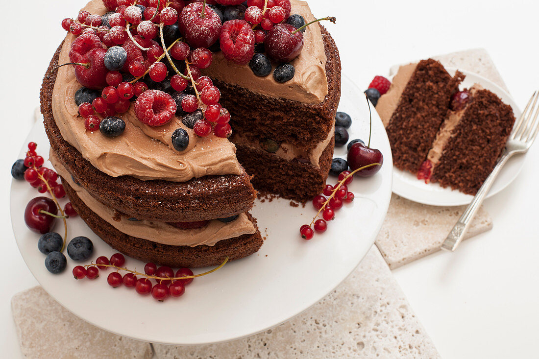 Frosted Chocolate Layer Cake decorated with fresh berries, on white cake stand