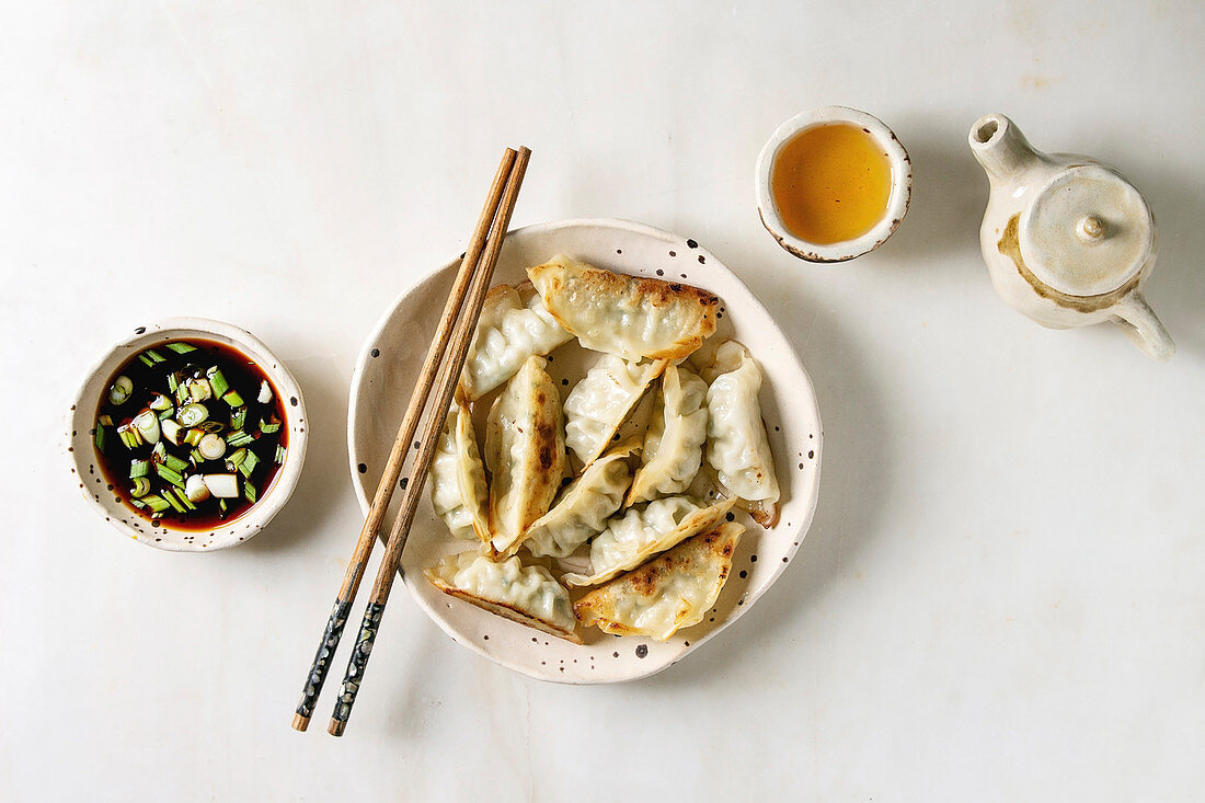 Fried asian dumplings Gyozas potstickers in white ceramic plate, bowl of soy onion sauce and teapot