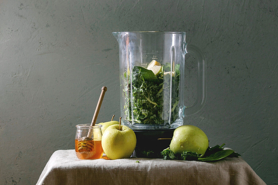 Ingredients for green spinach kale apple honey smoothie in glass blender and ingredients