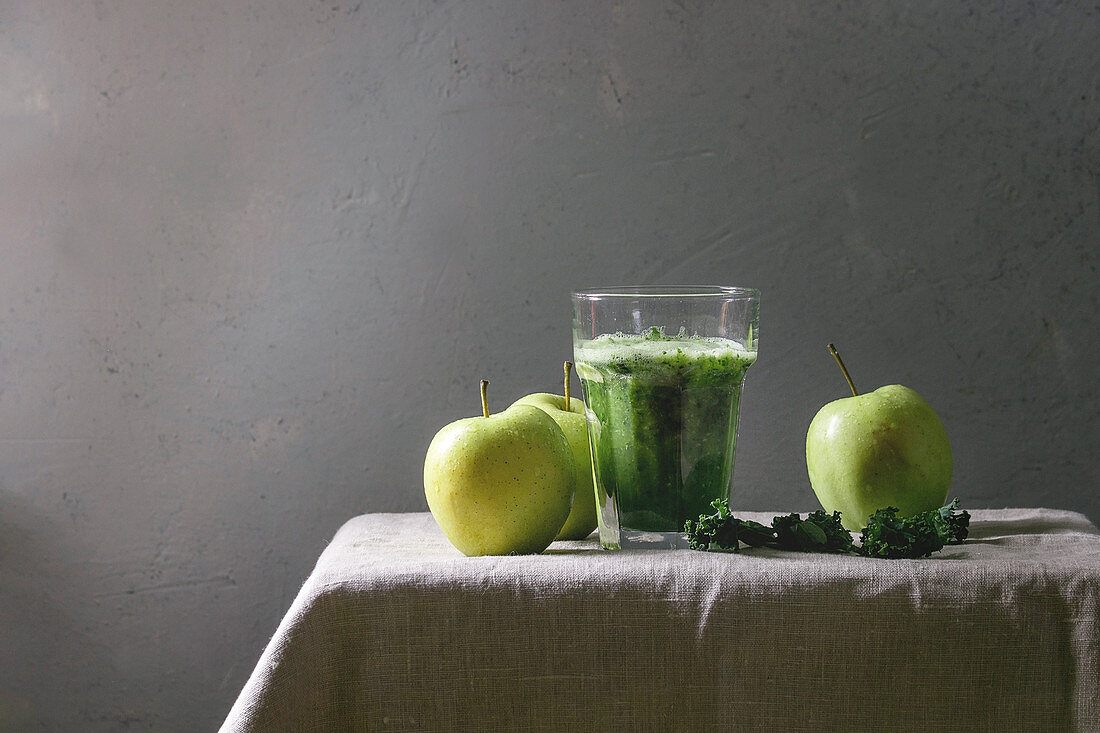 Green spinach kale apple smoothie in glass on linen table cloth with ingredients above