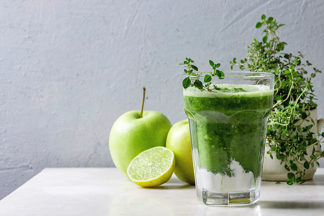 Green spinach kale apple honey smoothie in glass on white marble table with blender and ingredients above