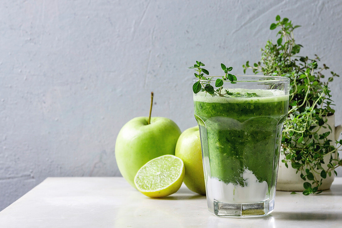Grüner Smoothie mit Spinat, Kohl und Apfel im Glas, dahinter Zutaten