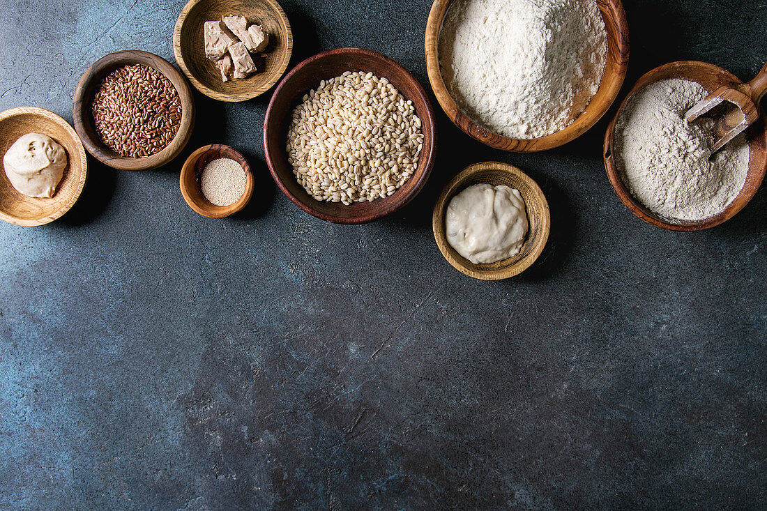 Ingredients for baking bread. Variety of wheat and rye flour, grains, yeast, sourdough over dark blue texture background