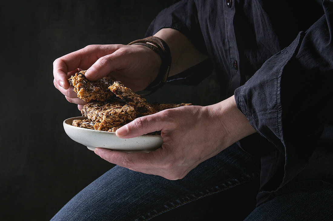 Woman holding ceramic plate with homemade energy oats granola bars with dried fruits and nuts