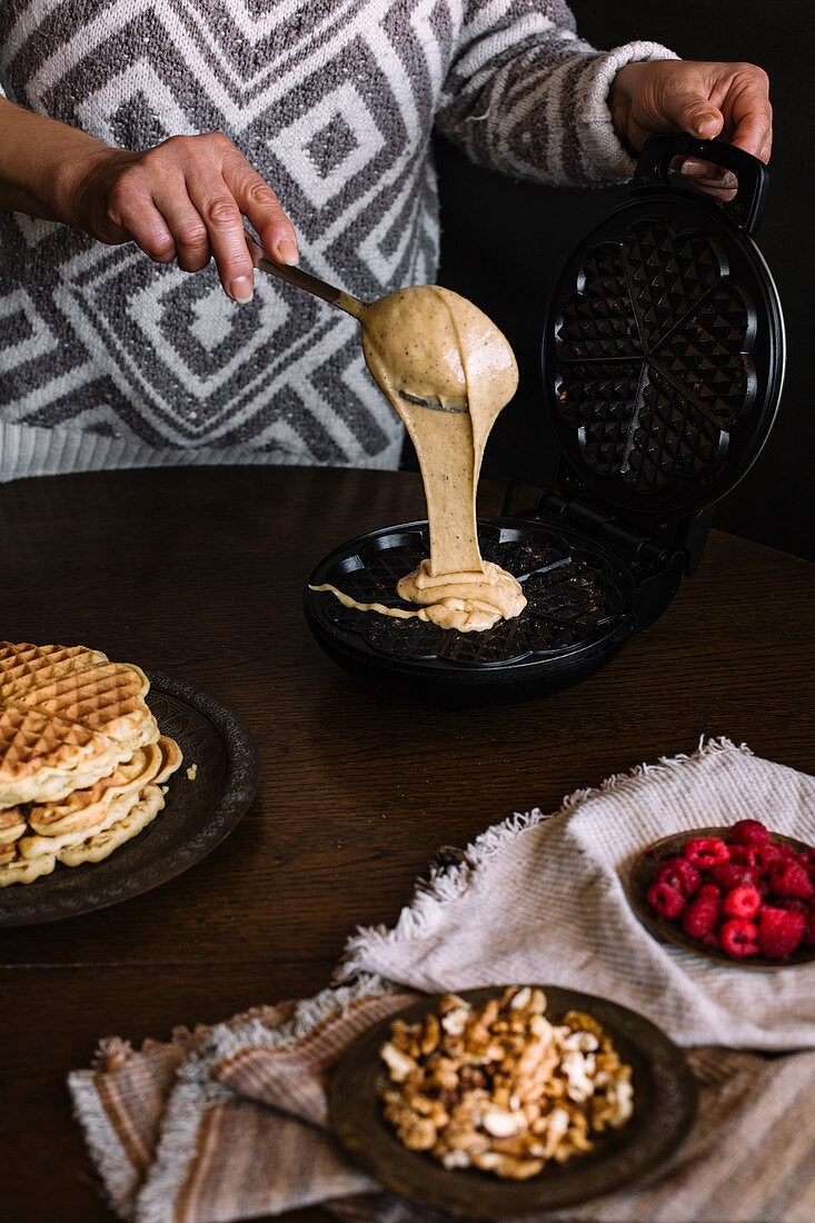 Woman is pouring dough on waffle maker