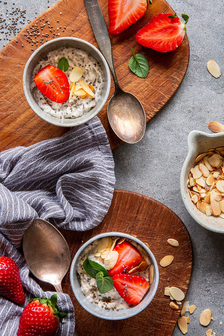 Chia pudding with strawberries, almonds and mint on brown wooden boards over grey concrete background