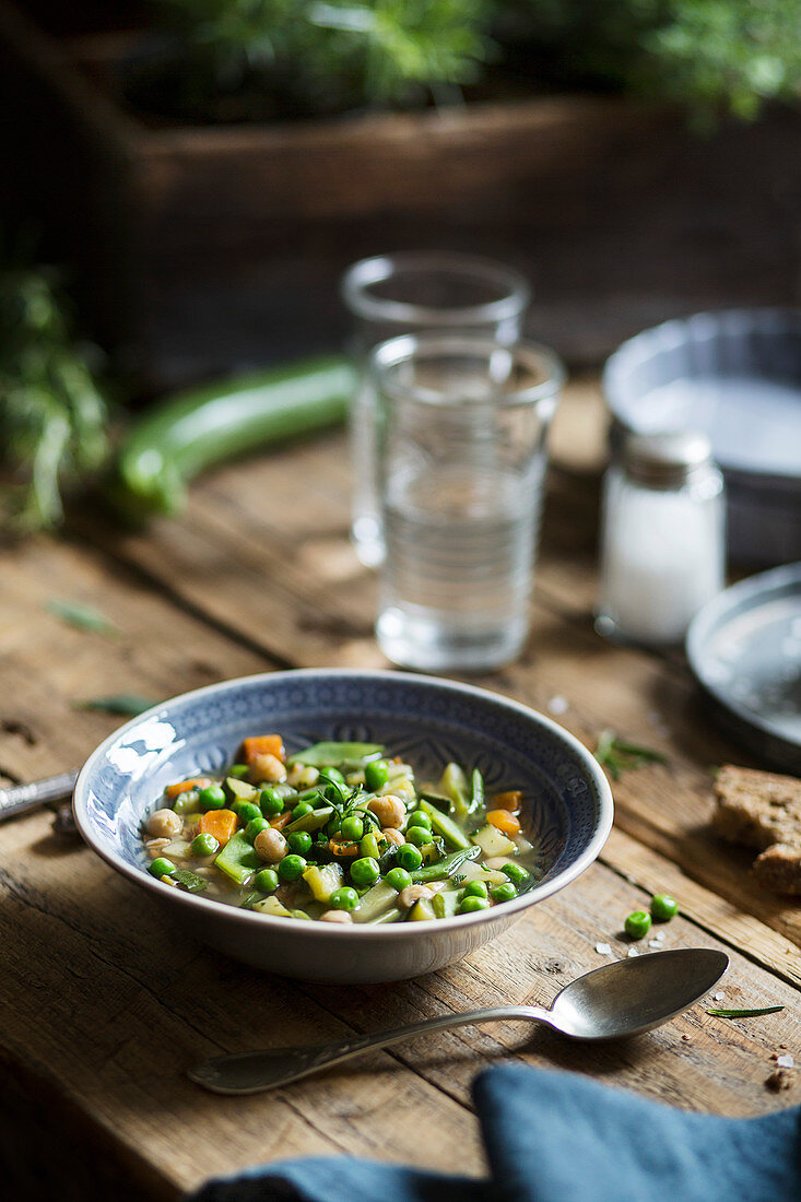 Soup with peas, carrots, zucchini and chickpeas on a rustic table