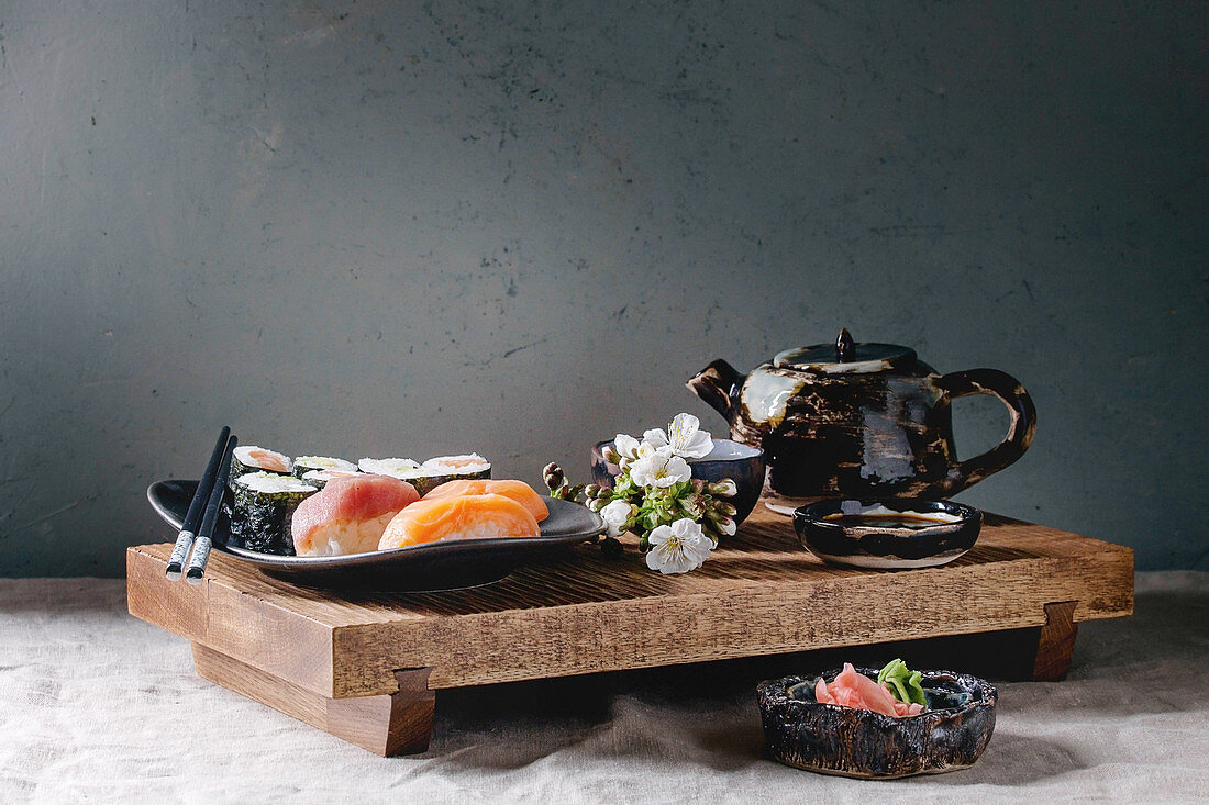 Sushi Set nigiri and sushi rolls on japanese wooden serving board with soy sauce, chopsticks, ceramic tea pot