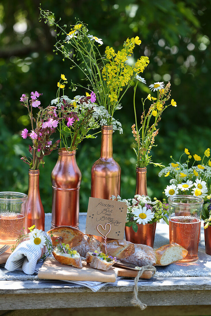 Baguette with floral butter on table decorated with wildflowers in copper-coloured containers
