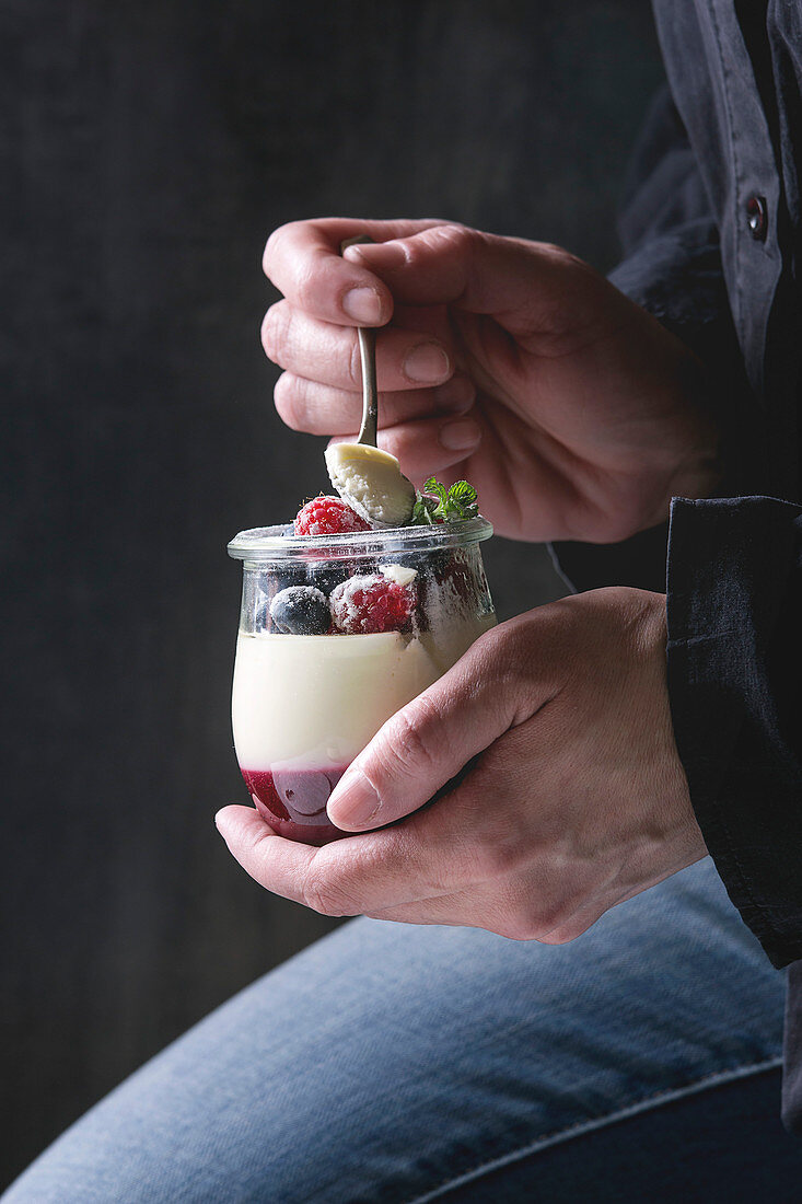 Woman holding in hands homemade classic dessert Panna cotta with raspberry and blueberry berries and jelly in jars