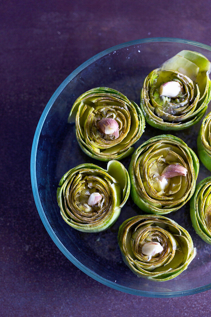 Plate of tasty ripe artichokes with aromatic garlic placed on violet tabletop