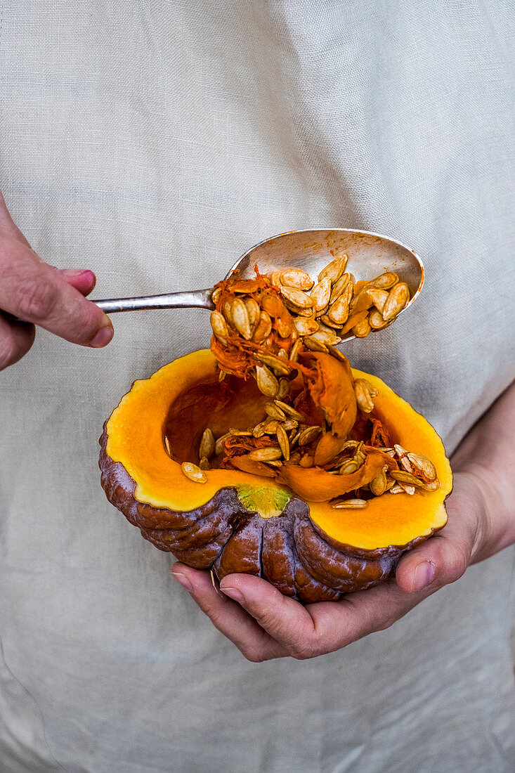 Person using silver tablespoon to remove seed from a pumpkin