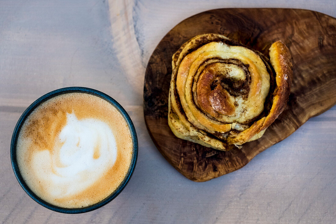A freshly baked cinnamon bun and a cup of cappuccino