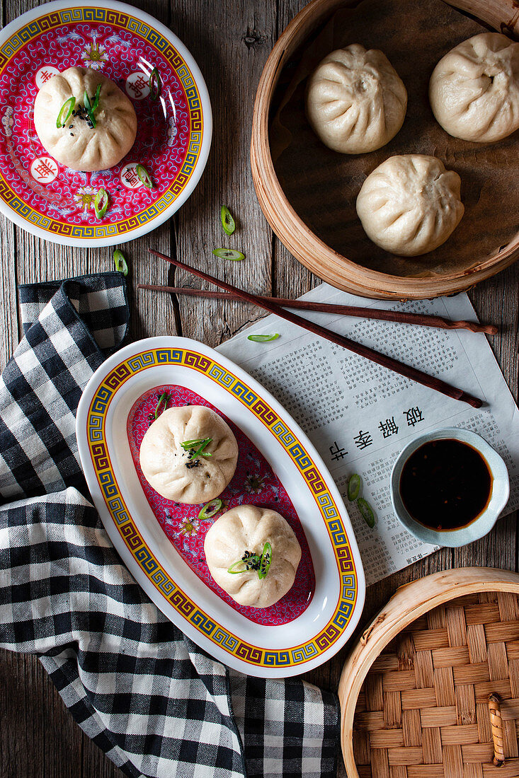 Chinesische Baozi (gedämpfte, gefüllte Teigtaschen) auf Tellern und in Dampfkörbchen