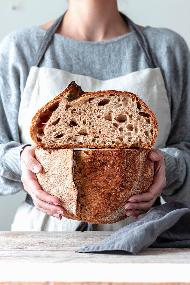 Hands of woman in kitchen apron holding both hands cutting homemade bread