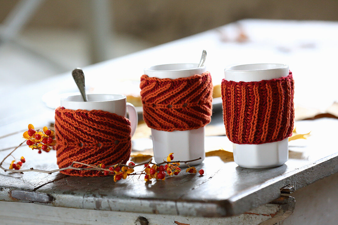 Rusty-red hand-knitted mug warmers for decorating autumnal table