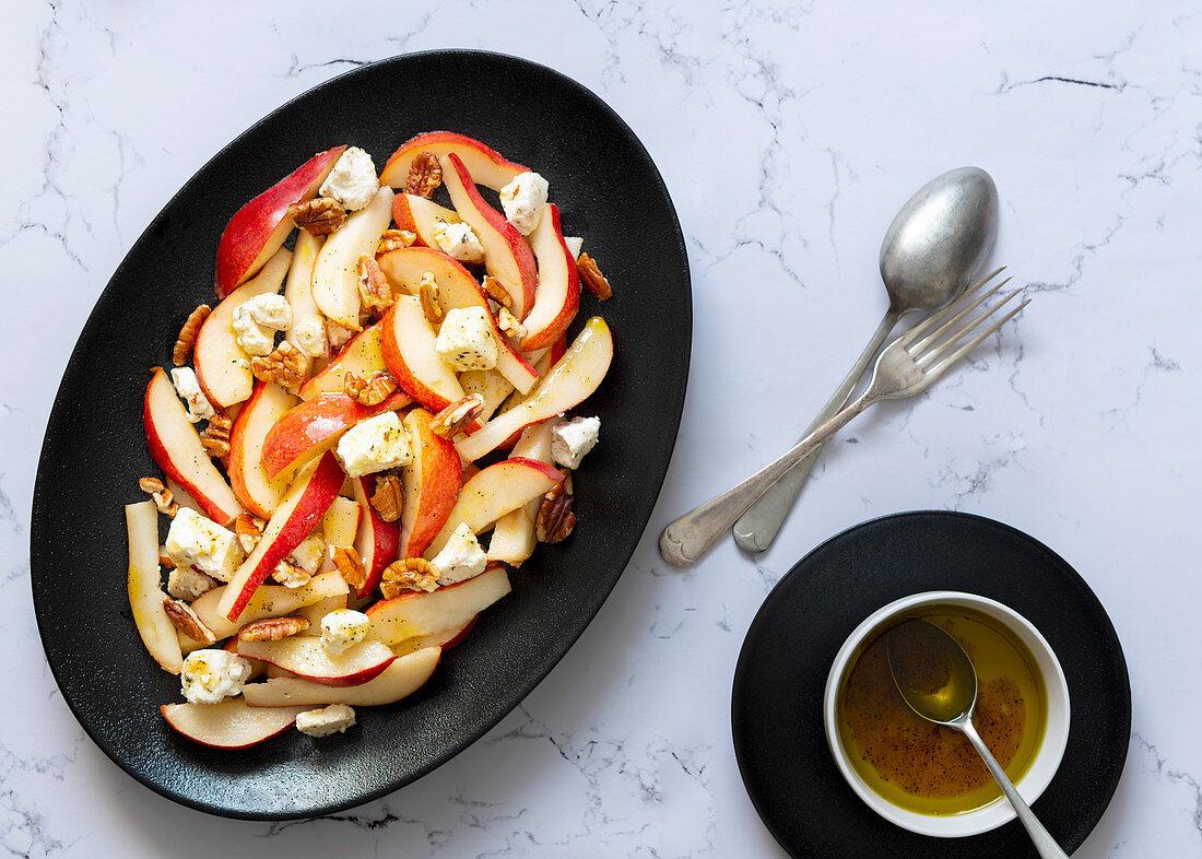 Sliced pears, blue vein cheese and walnuts covered with dressing on a black serving dish