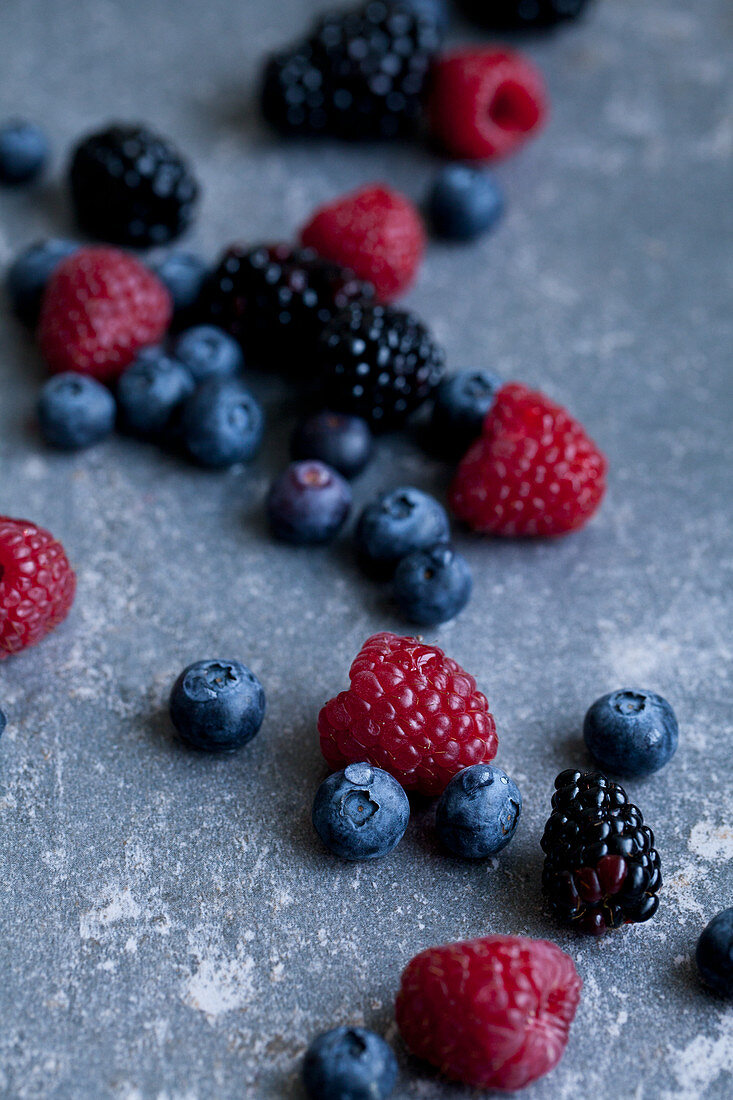 Raspberries, blackberries and blueberries with water droplets, photographed on a blue surface
