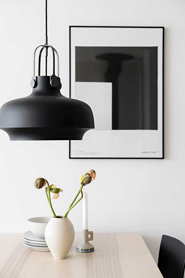 Vase of poppies on table below black pendant lamp