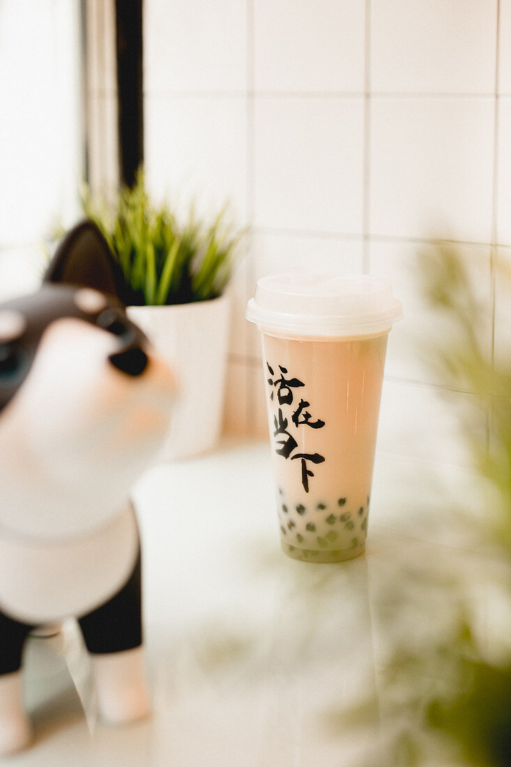 Tasty milk bubble tea with tapioca pearls in plastic cup on table in traditional Taiwanese cafe