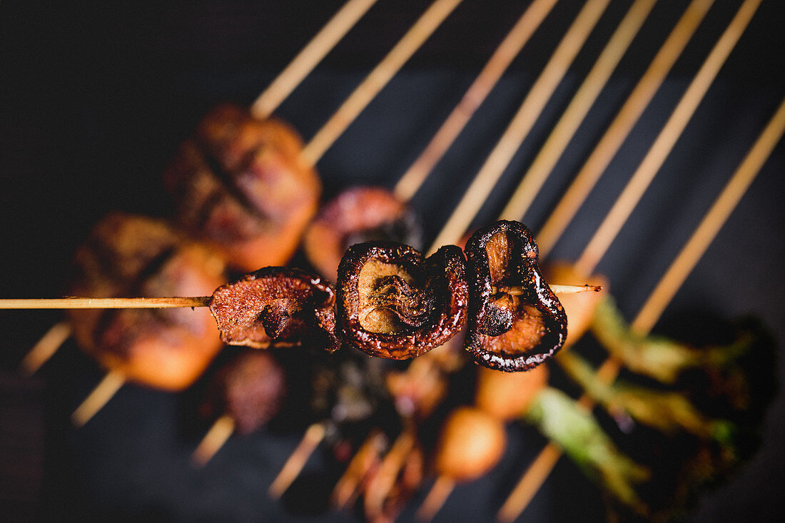 Cooked hot mushroom skewer over table with delicious grilled skewers with meat, fish, squid and broccoli