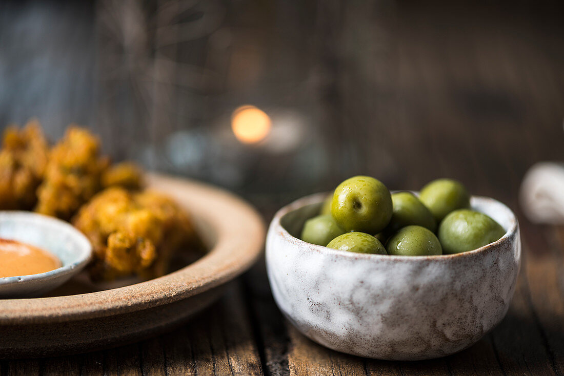 Green olives in a bowl, with chicken crispies and a dip