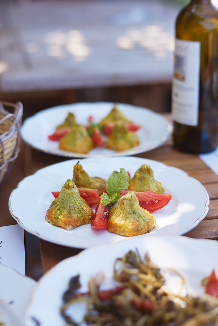 Dinner table with plates of filled zuchini flowers and tomatoes