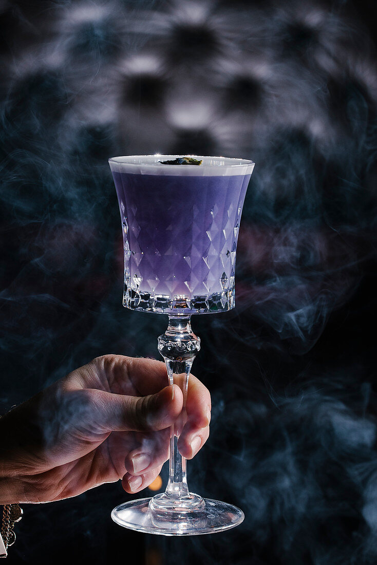 A hand holding a purple cocktail