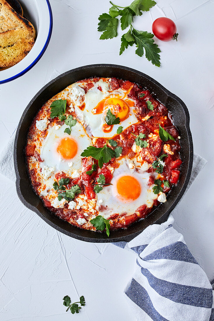 Shakshuka with tomatoes, peppers, onions and eggs prepared in cast iron skillet